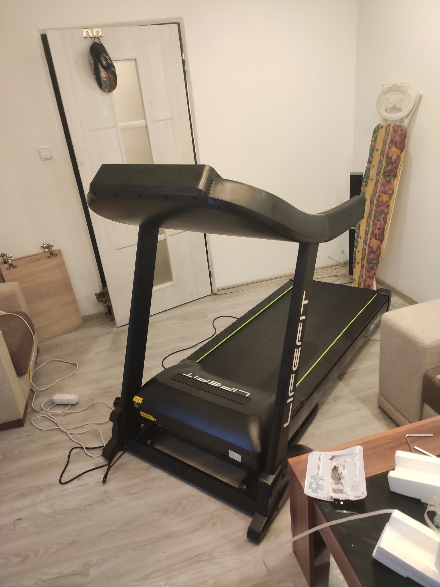 Čierny bežecký pás Lifefit práve zmontovaný v obývačke, okolo neho káble a haraburda — 8. jún 2020 poobede.