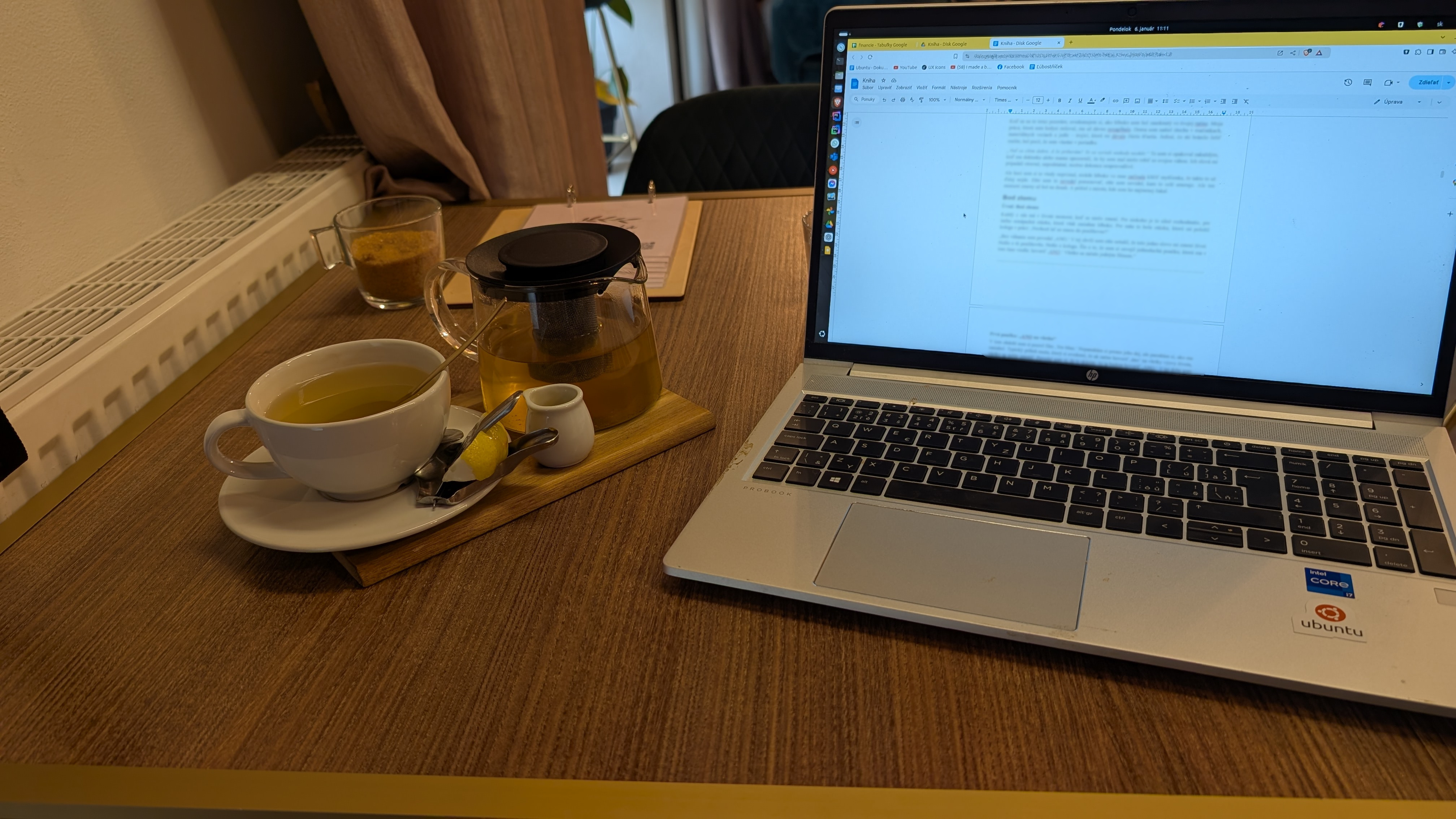 Stôl v kaviarni s čajom a notebookom, na obrazovke rukopis knihy, dátum 6. január, 11:11.
